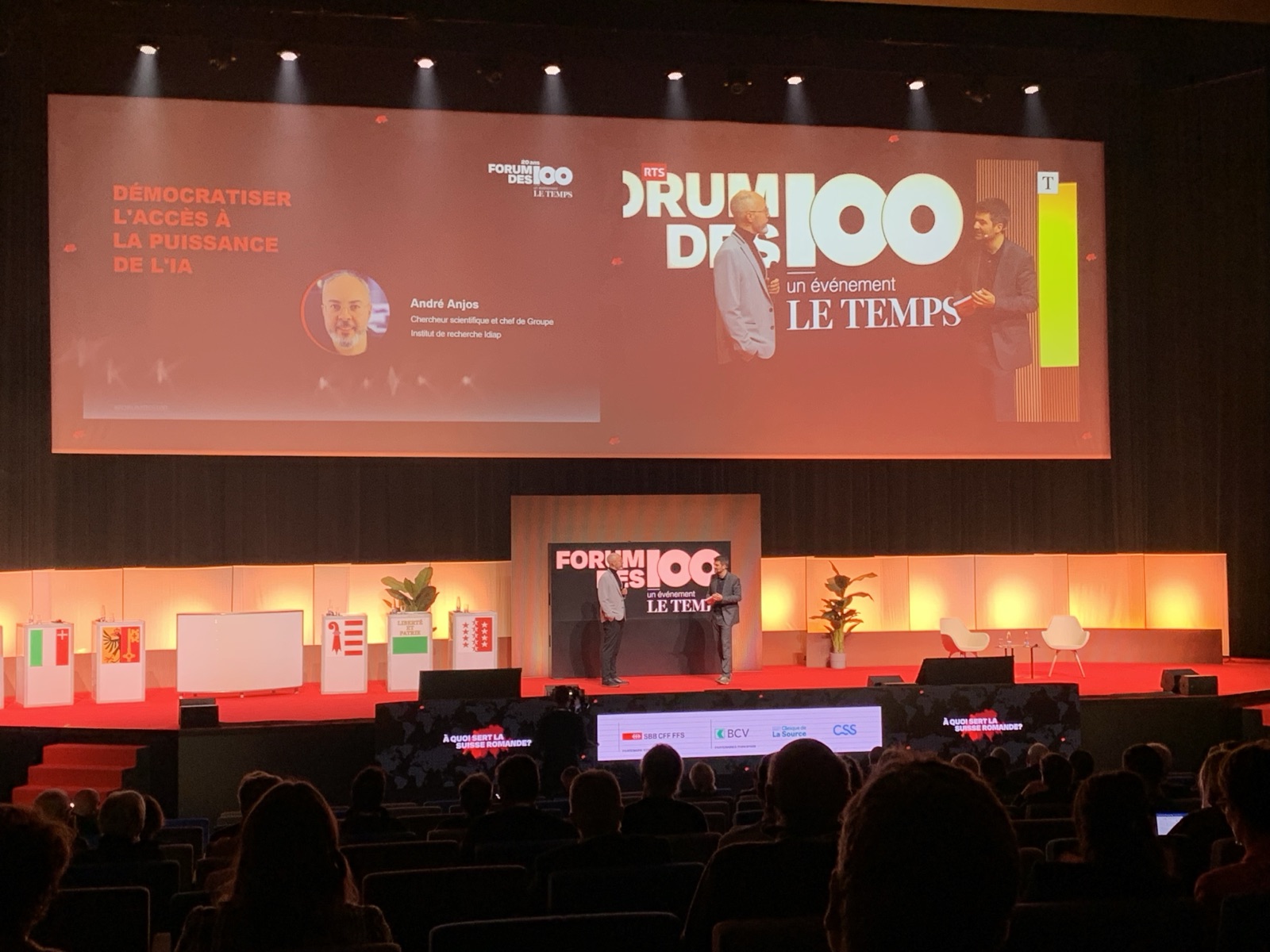 The Forum des 100 stage, with the title slide of the talk on the screen